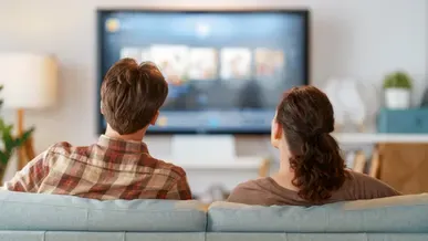A man and a woman sat on a sofa watching TV.